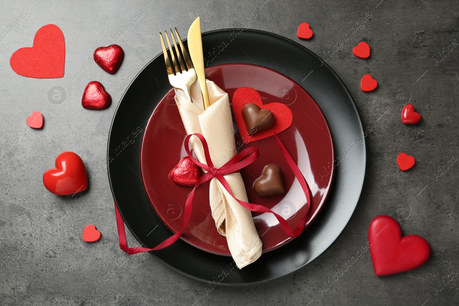 Photo of Romantic place setting for Valentine's day. Tableware, cutlery, candies and decorative hearts on grey textured table, flat lay