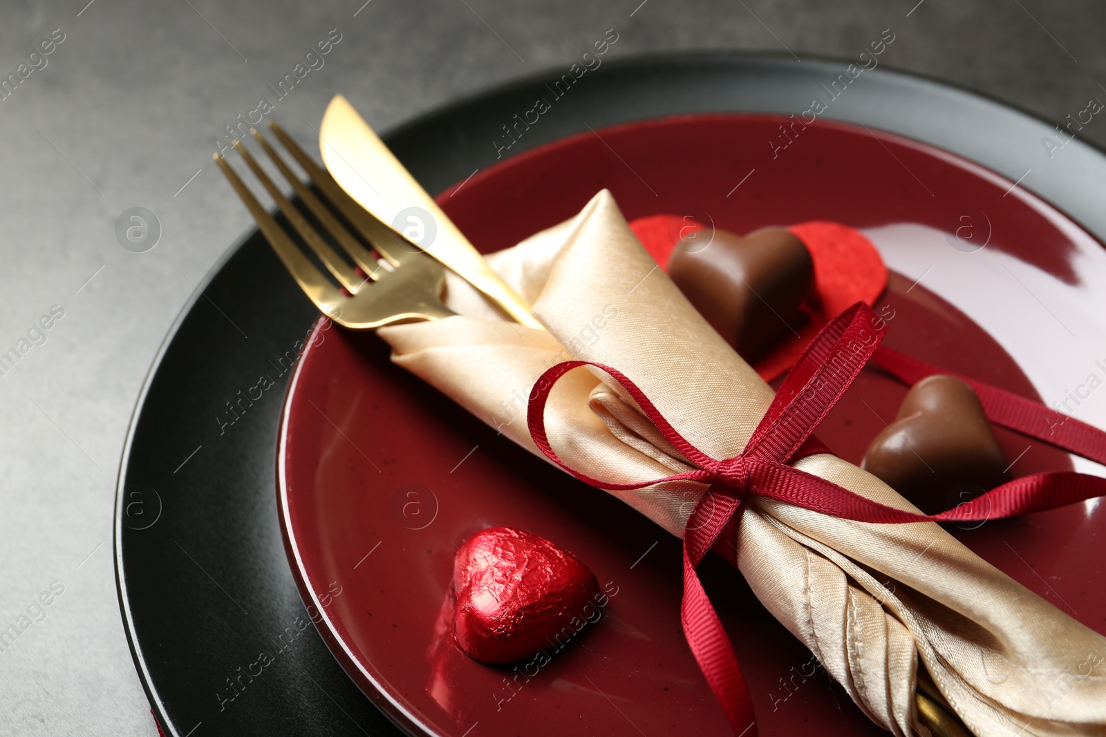 Photo of Romantic place setting for Valentine's day. Tableware, cutlery and candies in shape of hearts on grey table, closeup