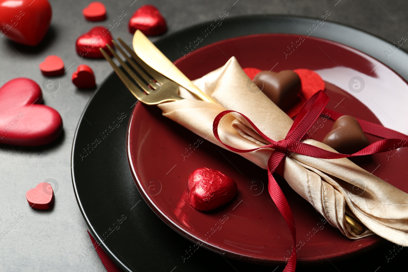 Photo of Romantic place setting for Valentine's day. Tableware, cutlery and candies in shape of hearts on grey table, closeup