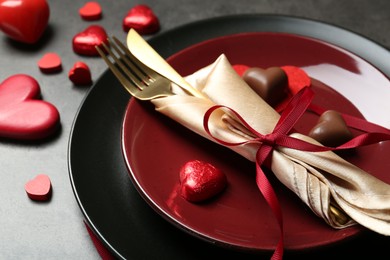 Romantic place setting for Valentine's day. Tableware, cutlery and candies in shape of hearts on grey table, closeup