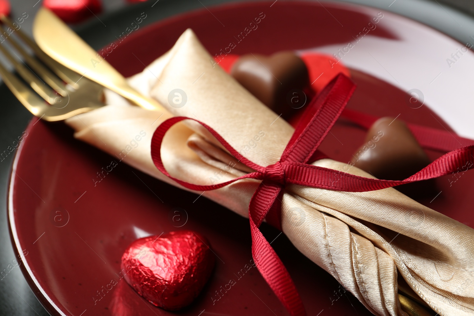 Photo of Romantic place setting for Valentine's day. Cutlery and candies in shape of hearts on plate, closeup