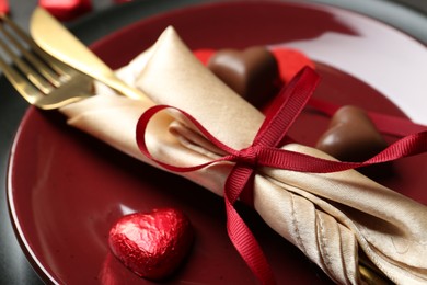 Photo of Romantic place setting for Valentine's day. Cutlery and candies in shape of hearts on plate, closeup