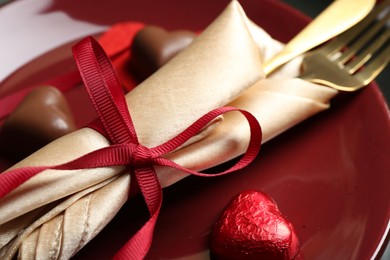 Photo of Romantic place setting for Valentine's day. Cutlery and candies in shape of hearts on plate, closeup