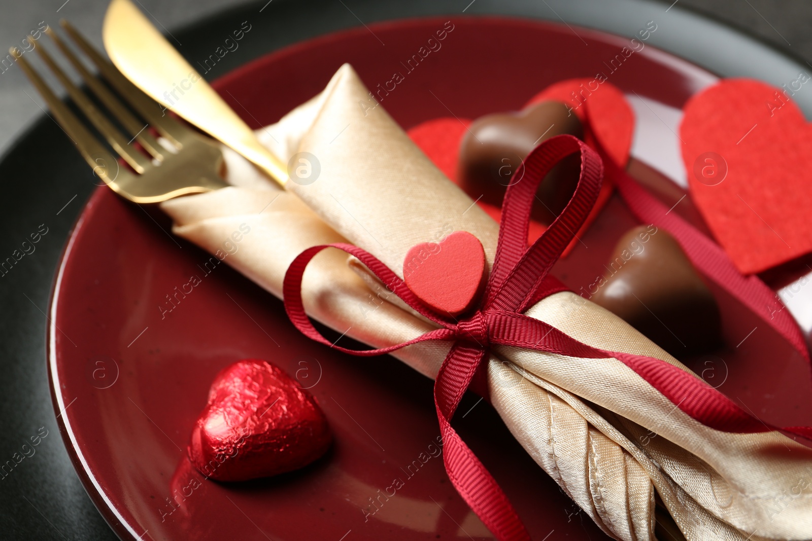 Photo of Romantic place setting for Valentine's day. Tableware, cutlery and candies in shape of hearts on table, closeup