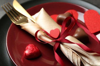 Romantic place setting for Valentine's day. Tableware, cutlery and candies in shape of hearts on table, closeup