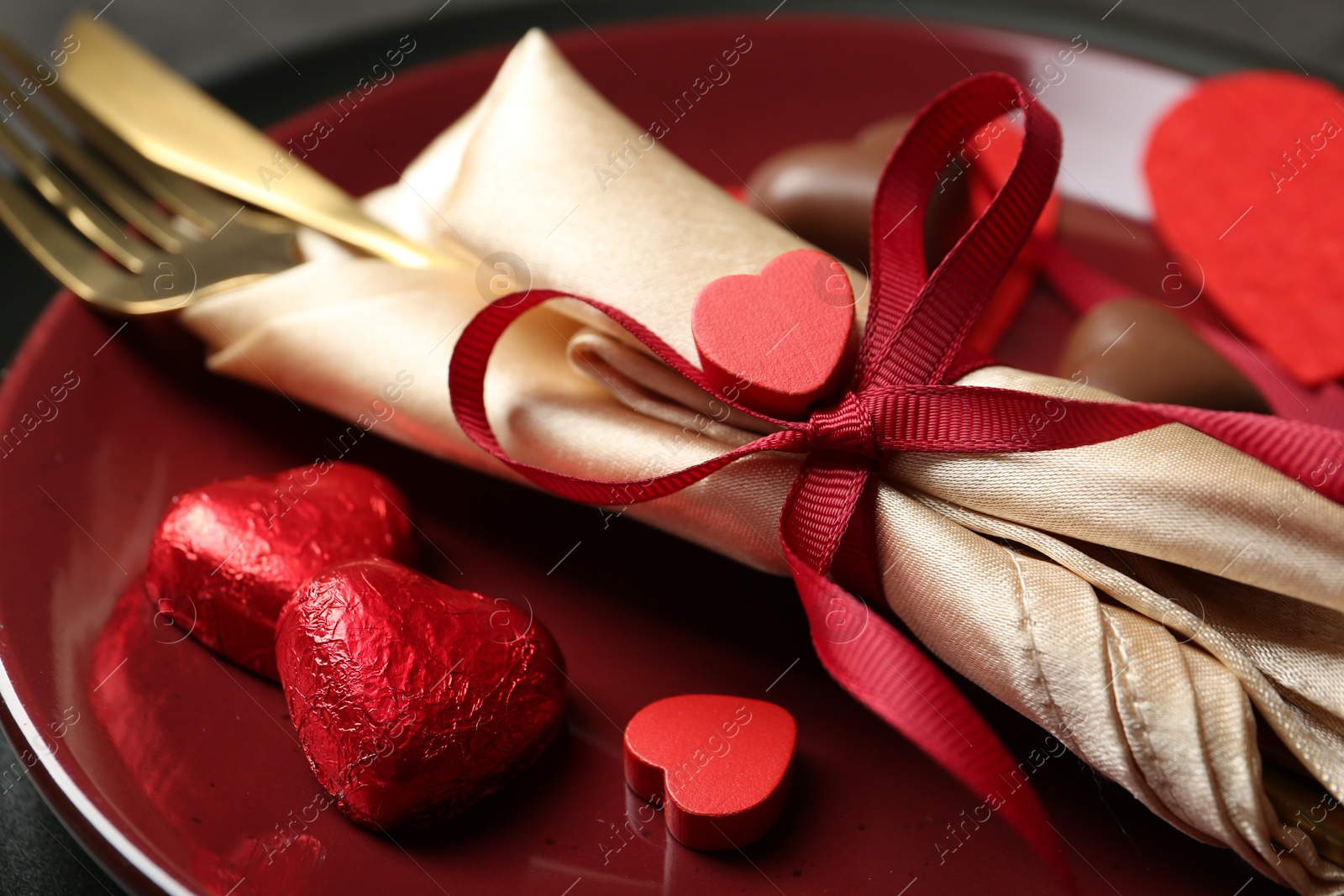 Photo of Romantic place setting for Valentine's day. Tableware, cutlery and candies in shape of hearts on table, closeup