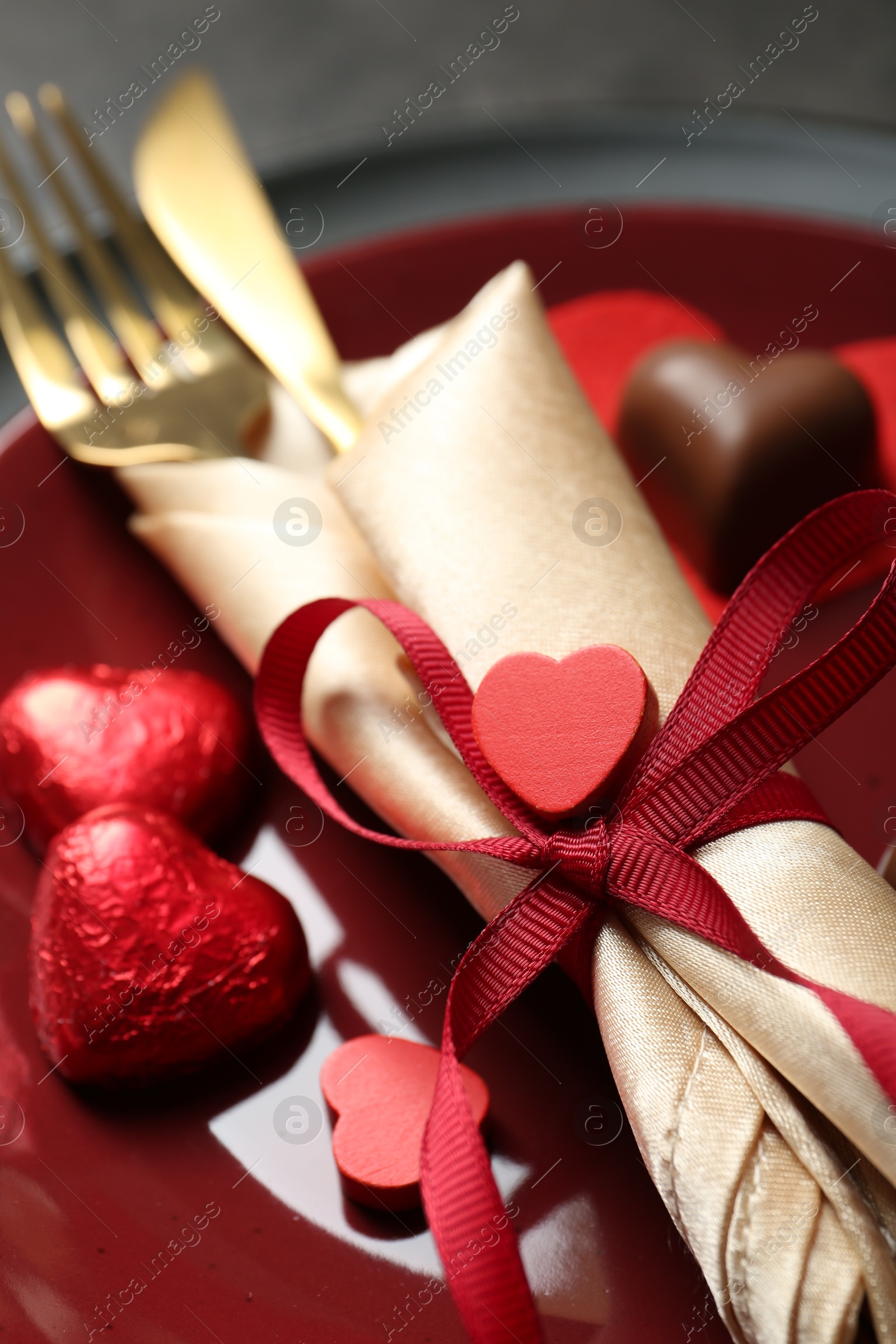 Photo of Romantic place setting for Valentine's day. Tableware, cutlery and candies in shape of hearts on grey table, closeup