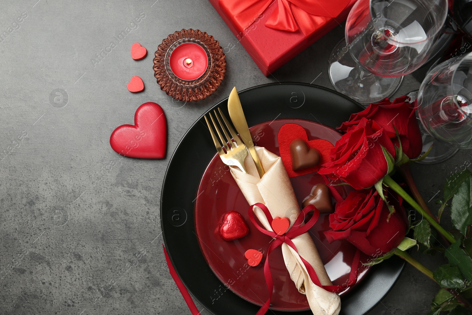 Photo of Romantic place setting for Valentine's day. Tableware, cutlery, candies, roses and decorative hearts on grey textured table, flat lay. Space for text