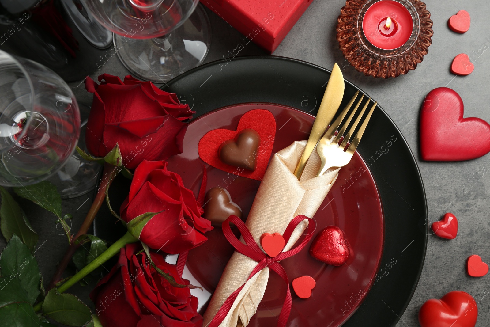 Photo of Romantic place setting for Valentine's day. Tableware, cutlery, candies, roses and decorative hearts on grey textured table, flat lay