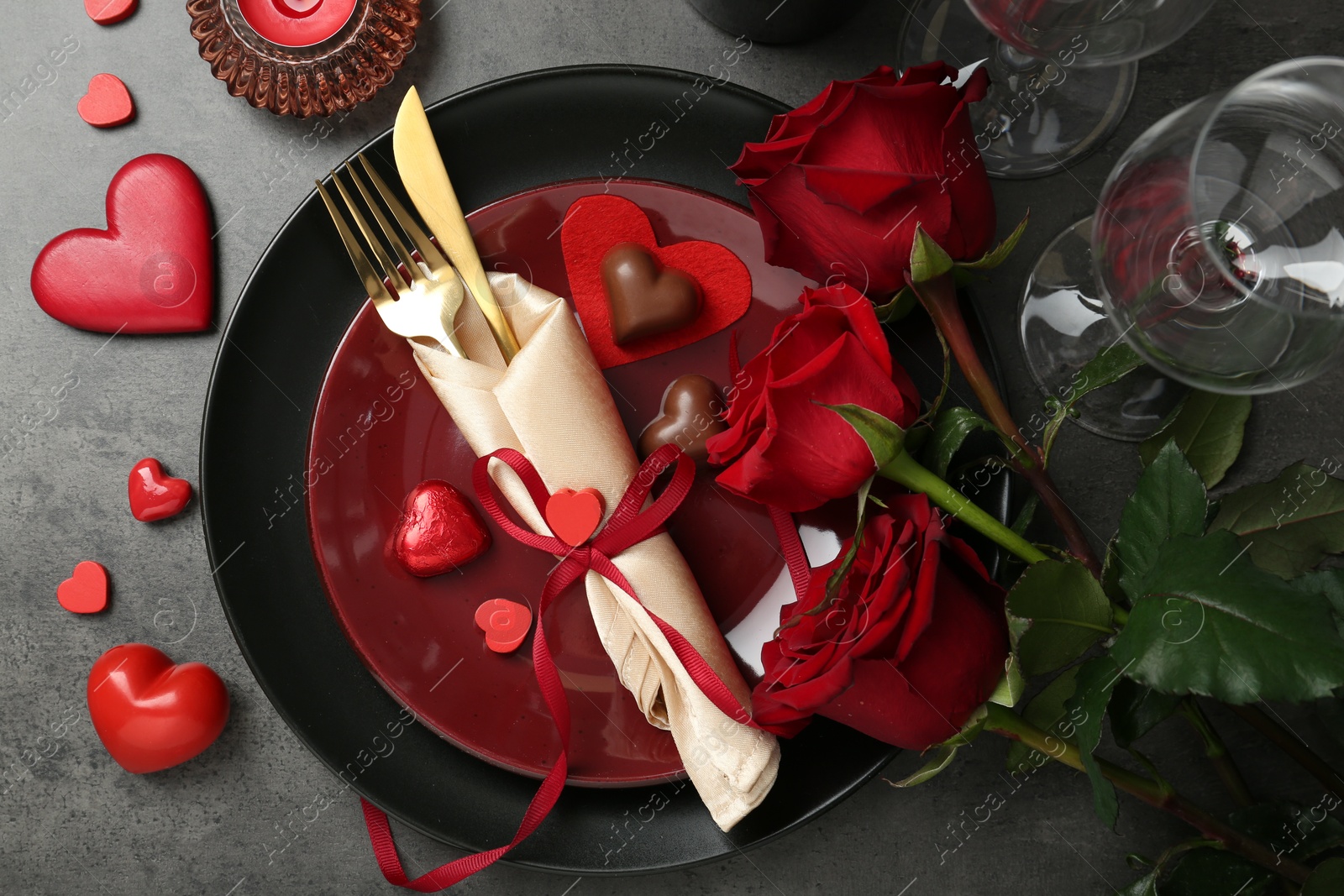 Photo of Romantic place setting for Valentine's day. Tableware, cutlery, candies, roses and decorative hearts on grey textured table, flat lay