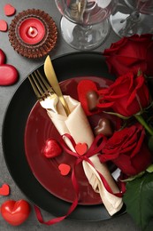 Photo of Romantic place setting for Valentine's day. Tableware, cutlery, candies, roses and decorative hearts on grey textured table, flat lay