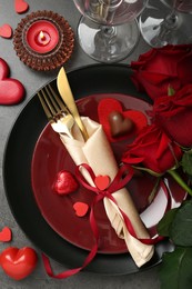 Romantic place setting for Valentine's day. Tableware, cutlery, candies, roses and decorative hearts on grey textured table, flat lay