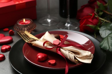 Photo of Romantic place setting for Valentine's day. Tableware, cutlery, candies, roses and decorative hearts on grey table, closeup