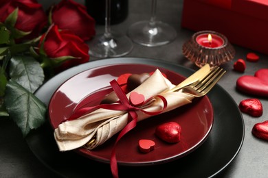 Photo of Romantic place setting for Valentine's day. Tableware, cutlery, candies, roses and decorative hearts on grey table, closeup