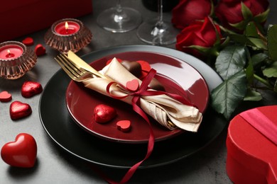 Photo of Romantic place setting for Valentine's day. Tableware, cutlery, candies, roses and decorative hearts on grey table, closeup