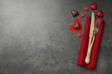 Photo of Romantic place setting for Valentine's day. Cutlery, candies and red decorative hearts on grey textured table, flat lay. Space for text