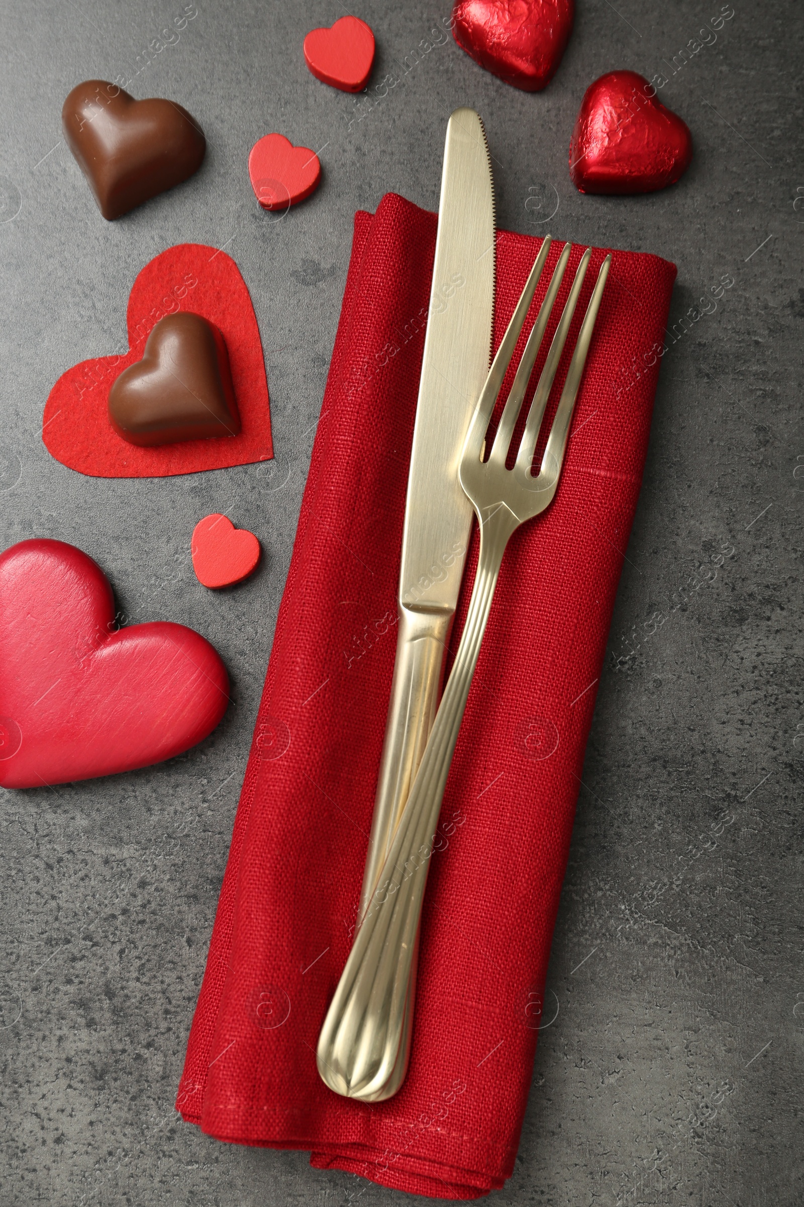 Photo of Romantic place setting for Valentine's day. Cutlery, candies and red decorative hearts on grey textured table, flat lay