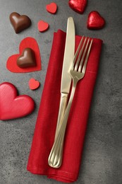 Photo of Romantic place setting for Valentine's day. Cutlery, candies and red decorative hearts on grey textured table, flat lay