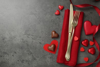 Photo of Romantic place setting for Valentine's day. Cutlery, candies and red decorative hearts on grey textured table, flat lay. Space for text