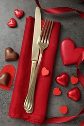 Romantic place setting for Valentine's day. Cutlery, candies and red decorative hearts on grey textured table, flat lay