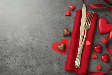 Photo of Romantic place setting for Valentine's day. Cutlery, candies and red decorative hearts on grey textured table, flat lay. Space for text