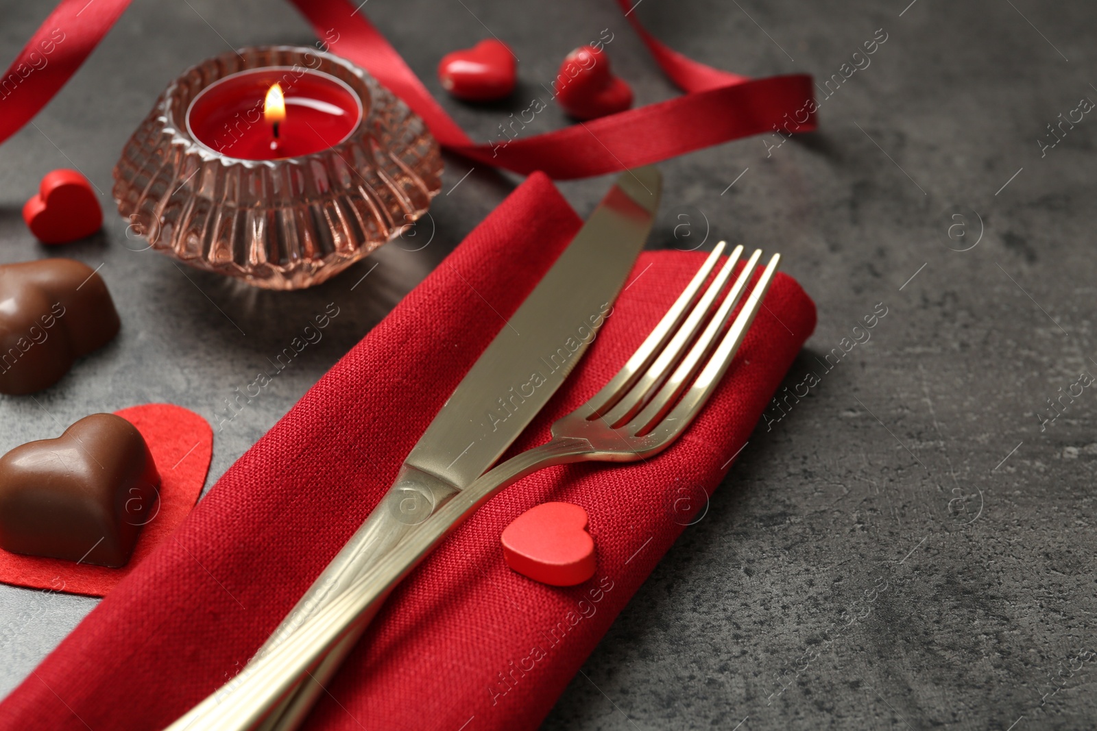 Photo of Romantic place setting for Valentine's day. Cutlery, candies, burning candle and decorative hearts on grey textured table, closeup