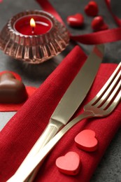 Photo of Romantic place setting for Valentine's day. Cutlery, candies, burning candle and decorative hearts on grey textured table, closeup