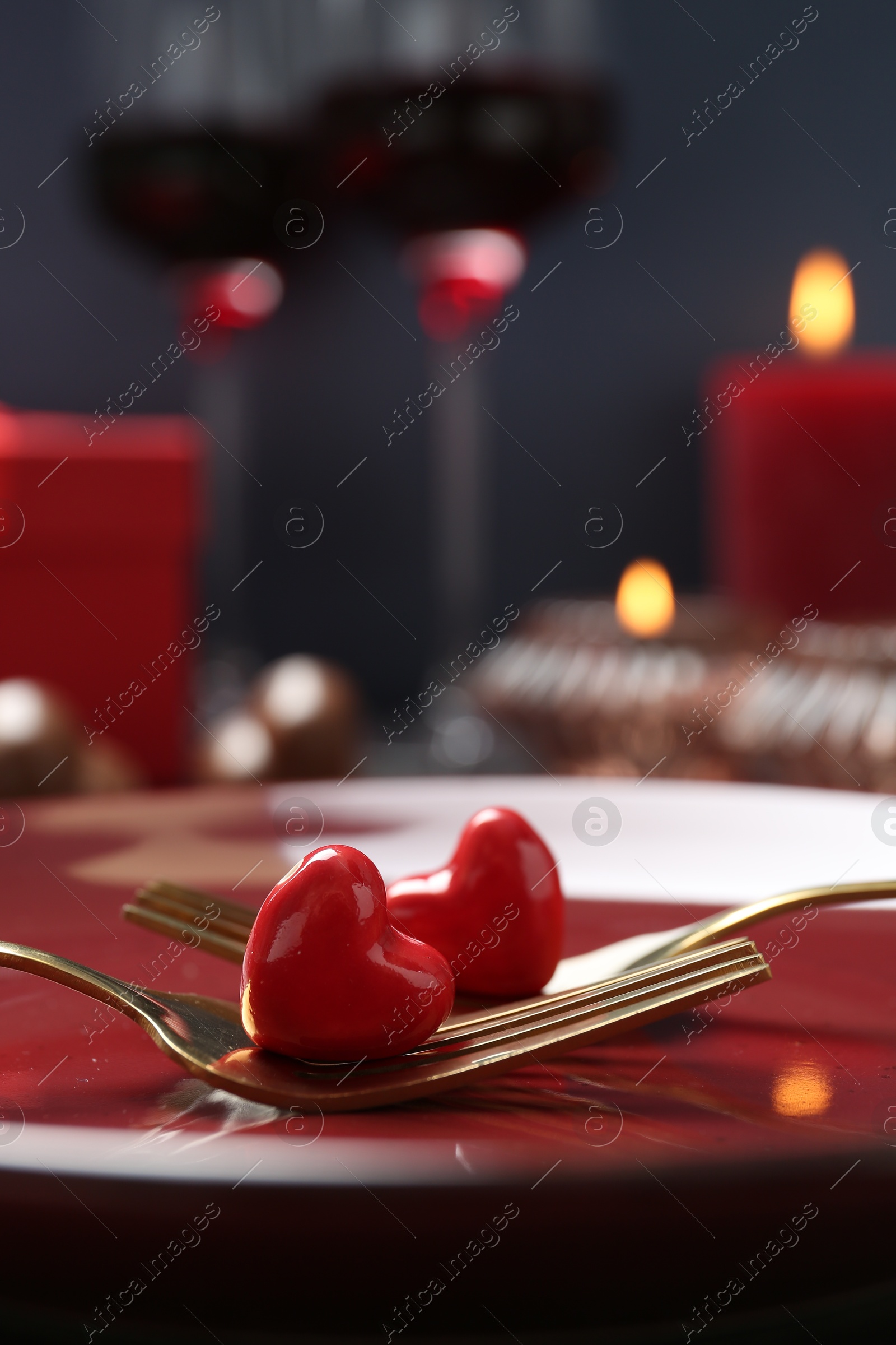 Photo of Romantic table setting for Valentine's day. Forks with decorative hearts on red plate, closeup