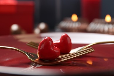 Photo of Romantic table setting for Valentine's day. Forks with decorative hearts on red plate, closeup