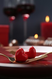 Photo of Romantic table setting for Valentine's day. Forks with decorative hearts on red plate, closeup