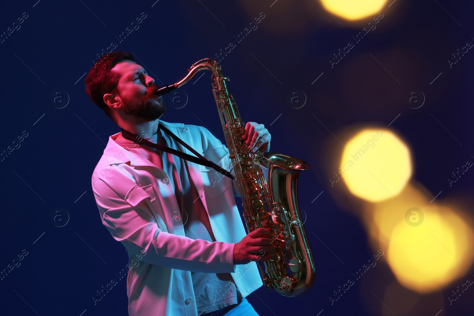 Photo of Professional musician playing saxophone on blue background with blurred lights. Bokeh effect