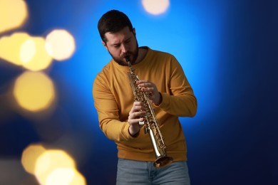 Photo of Professional musician playing soprano saxophone on blue background with blurred lights. Bokeh effect