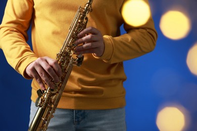 Photo of Professional musician holding soprano saxophone on blue background with blurred lights, closeup. Bokeh effect