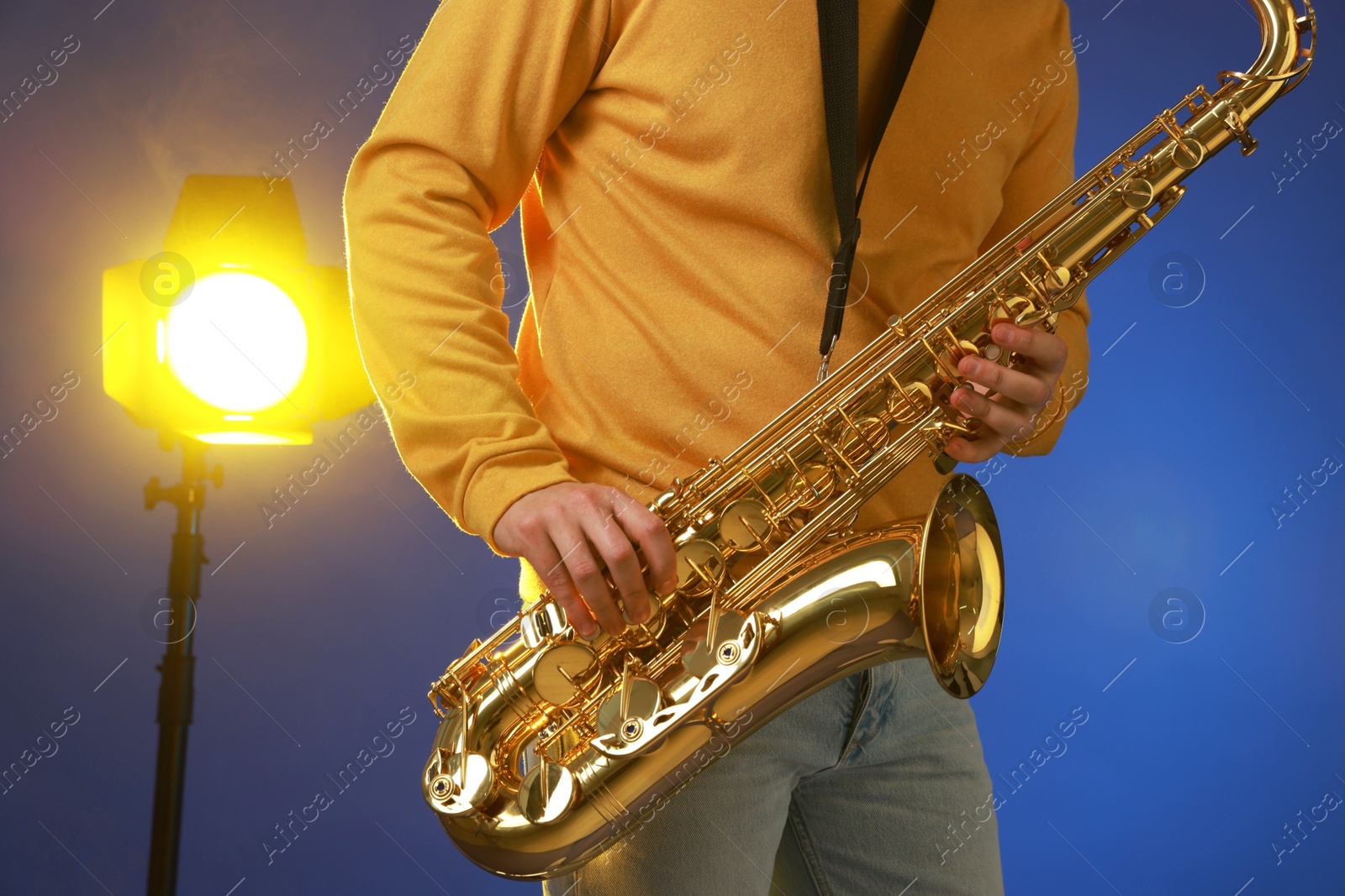 Photo of Professional musician playing saxophone on blue background with light, closeup