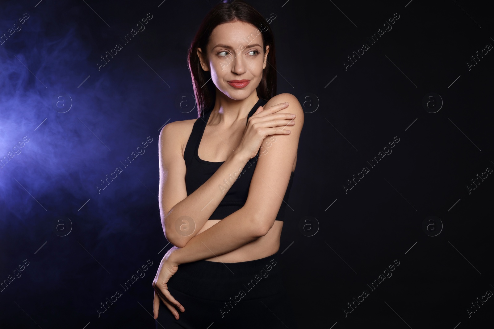 Photo of Beautiful woman in stylish sportswear on dark background with color light and smoke