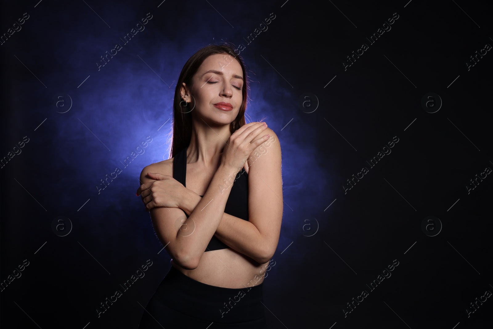 Photo of Beautiful woman in stylish sportswear on dark background with color light and smoke