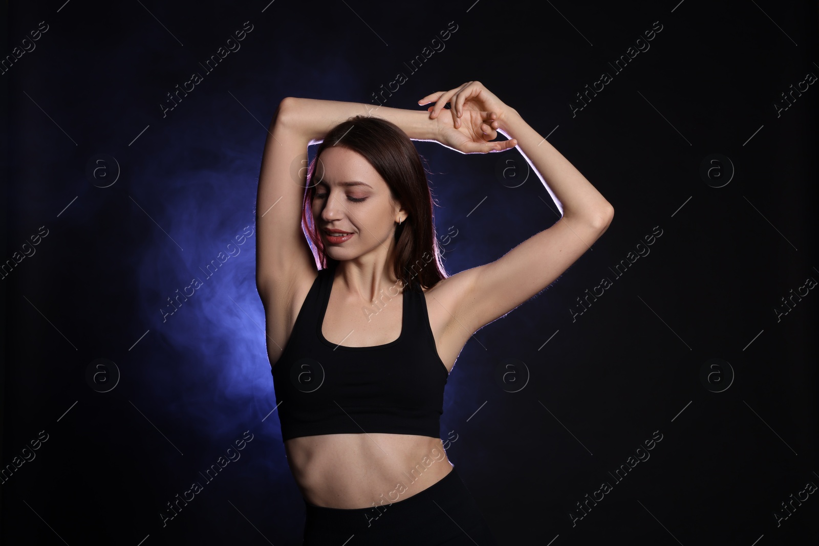 Photo of Beautiful woman in stylish sportswear on dark background with color light and smoke