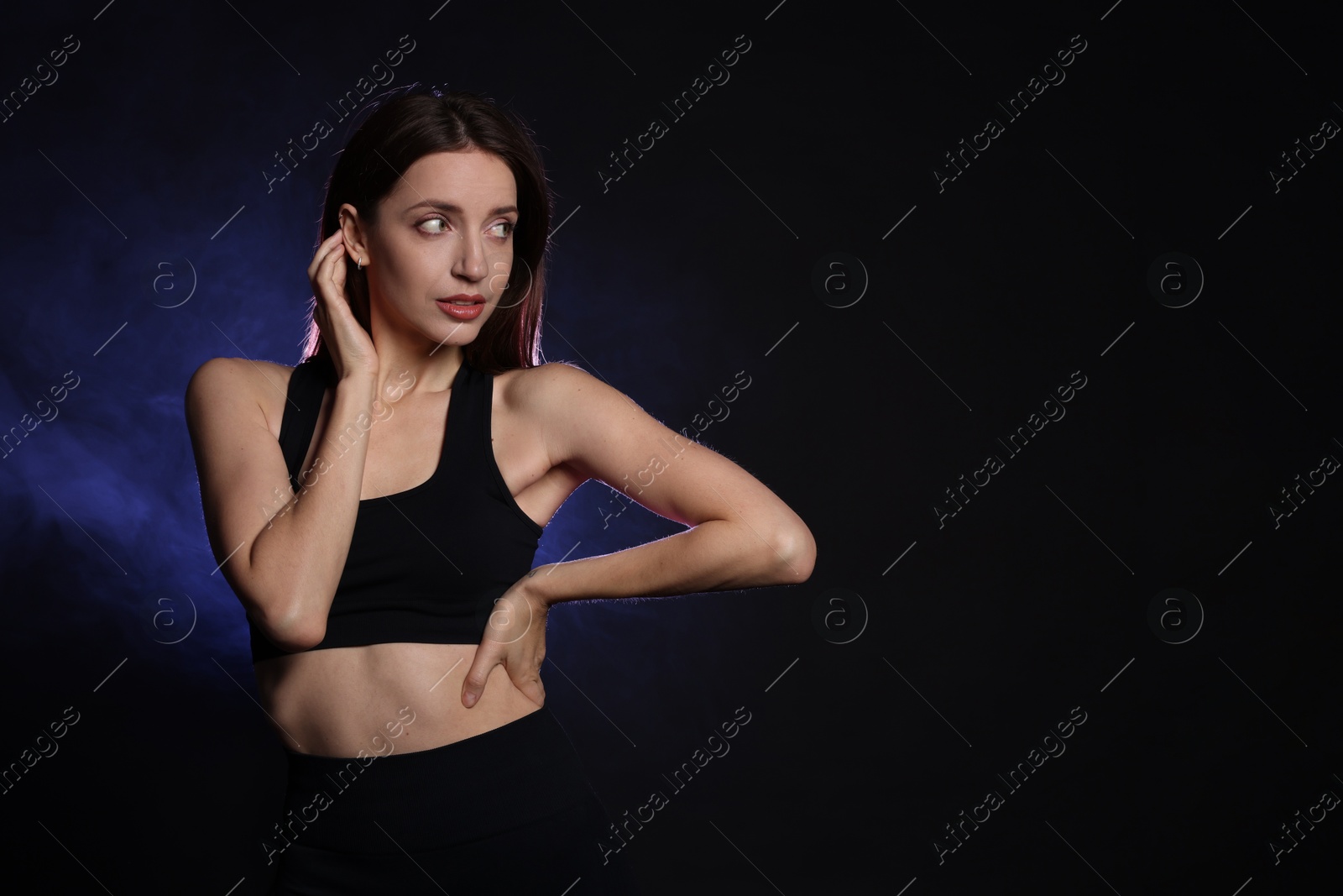 Photo of Beautiful woman in stylish sportswear on dark background with color light and smoke. Space for text