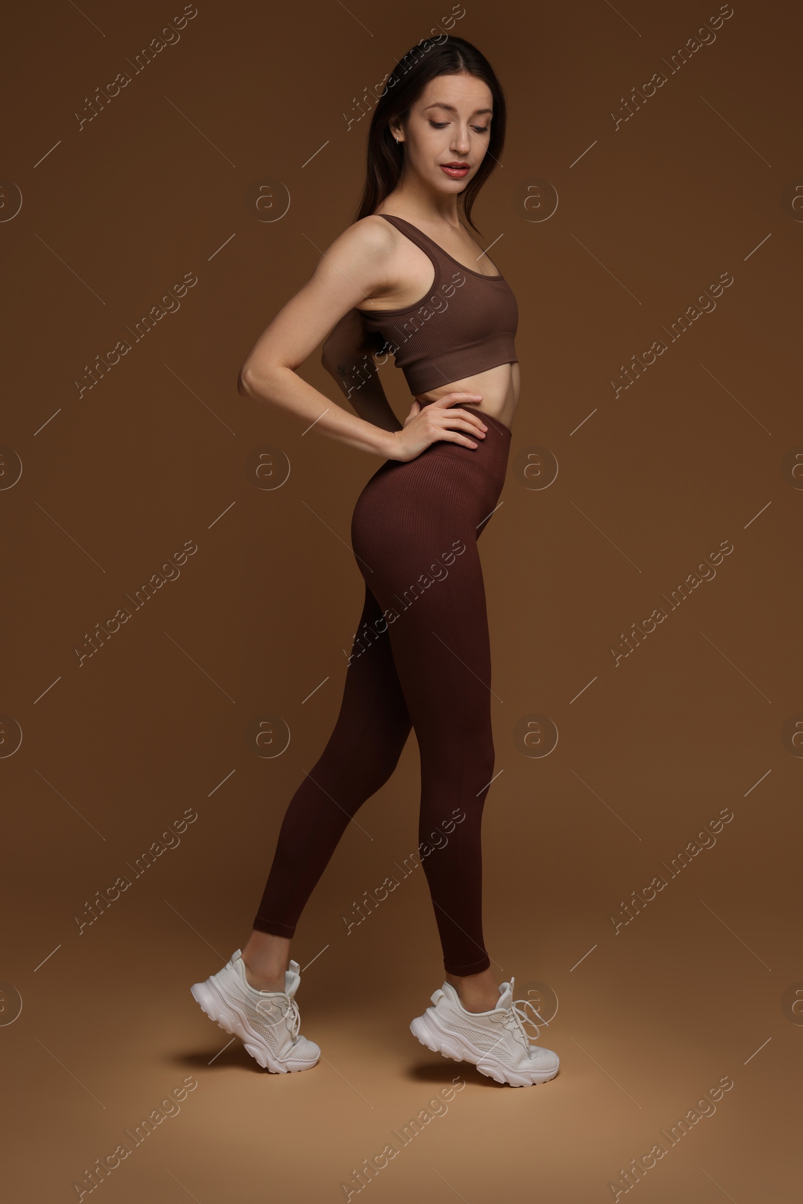 Photo of Beautiful woman in stylish sportswear on brown background