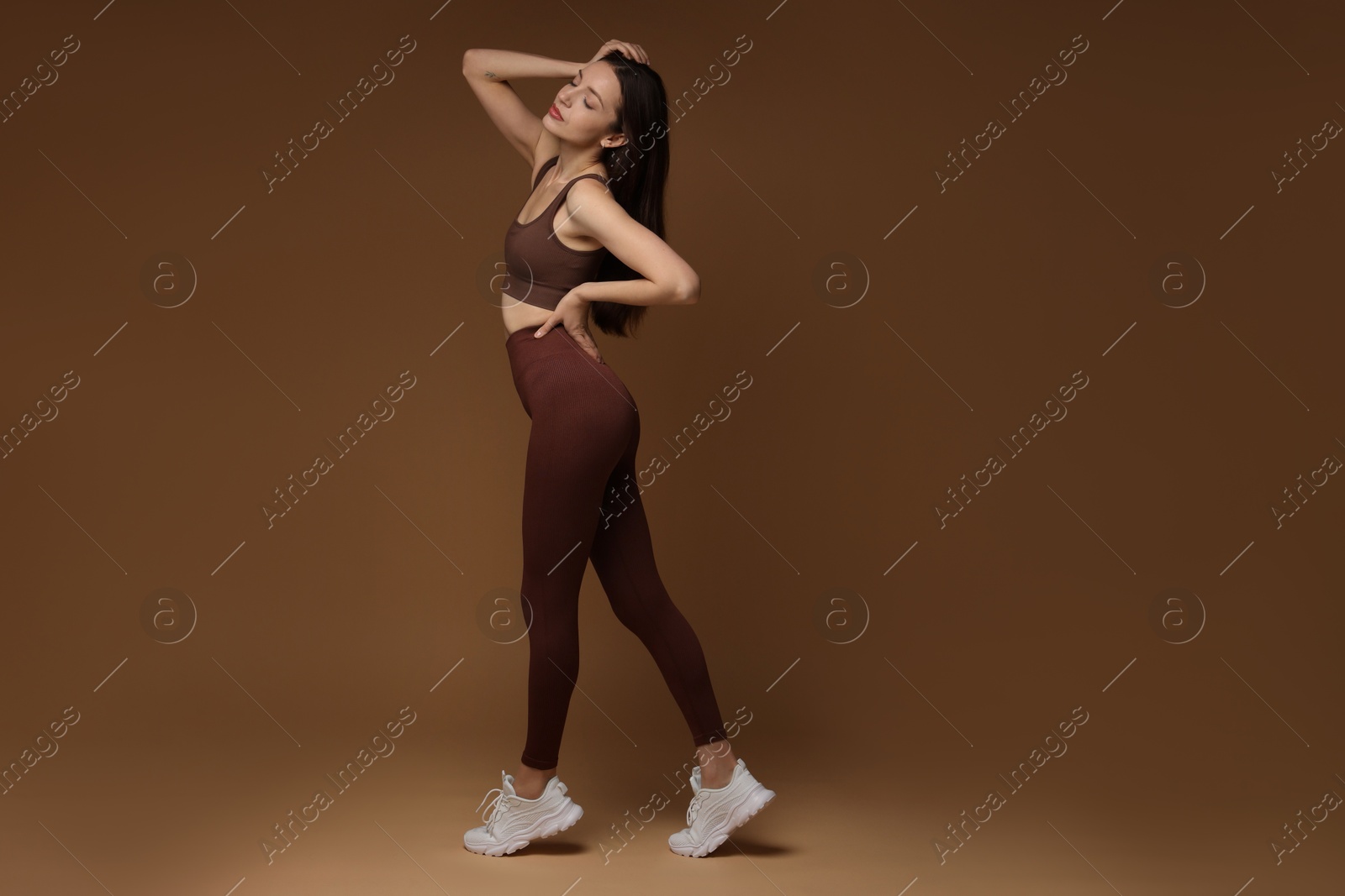 Photo of Beautiful woman in stylish sportswear on brown background