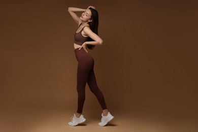 Photo of Beautiful woman in stylish sportswear on brown background