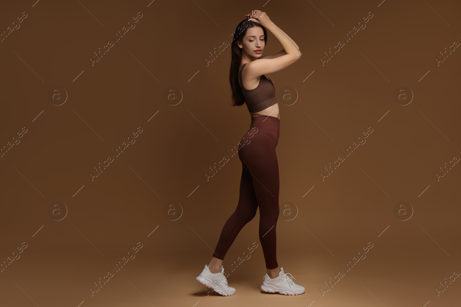 Photo of Beautiful woman in stylish sportswear on brown background