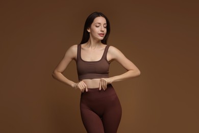 Photo of Beautiful woman in stylish sportswear on brown background