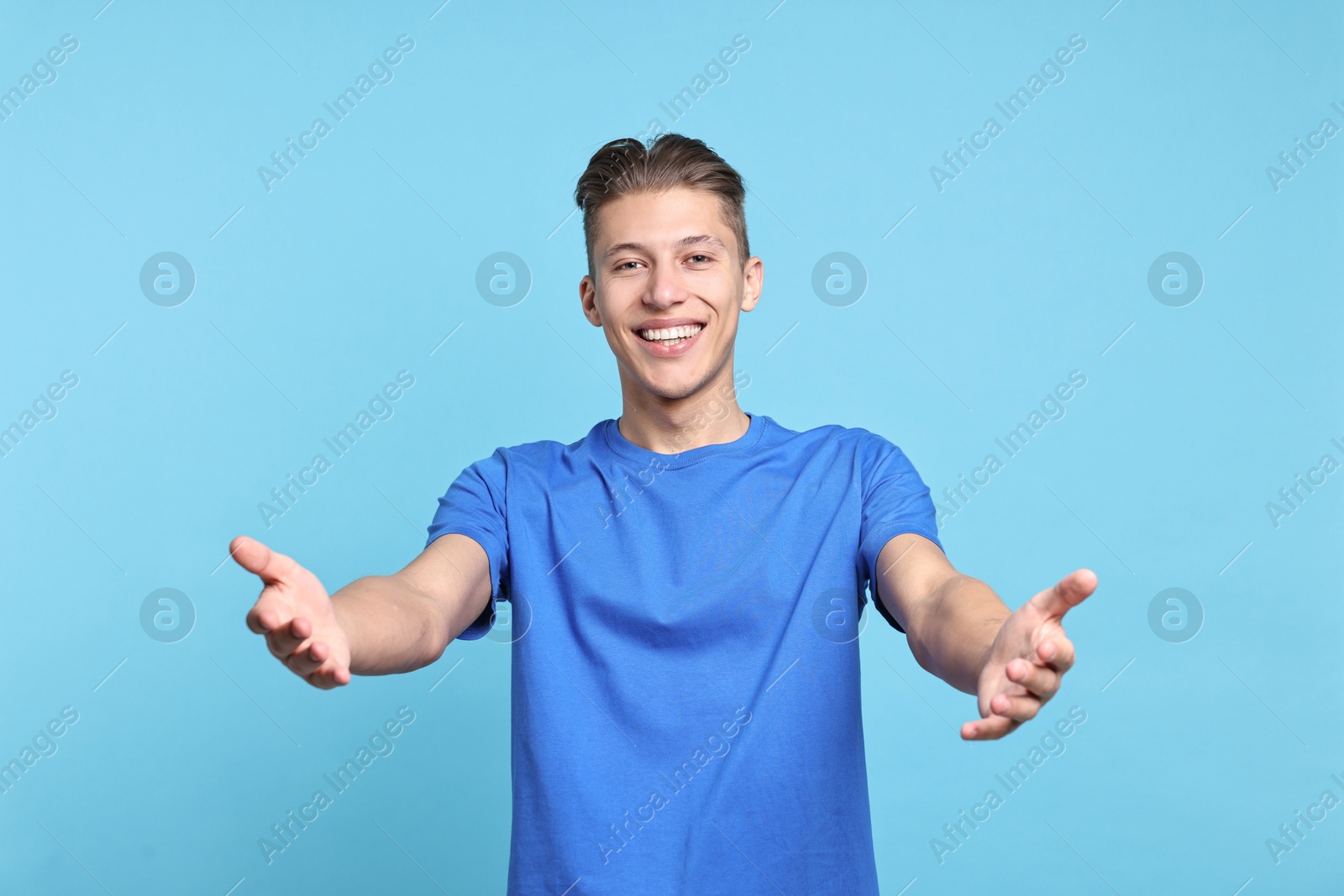 Photo of Happy man welcoming friends or guests on light blue background