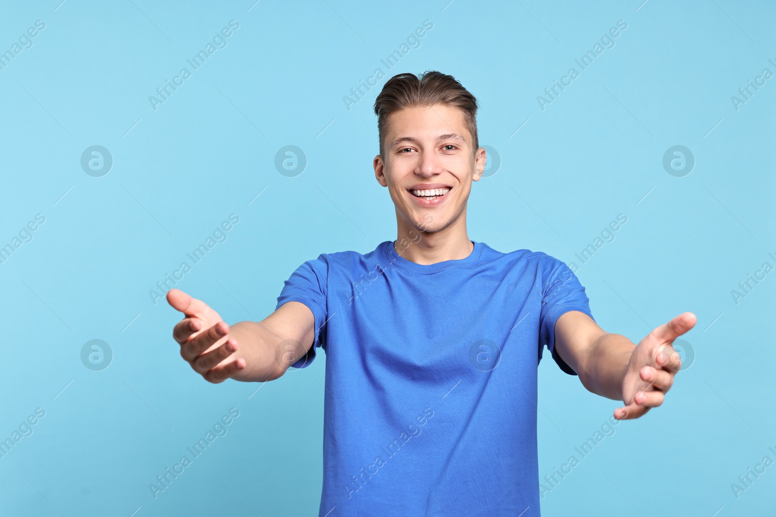 Photo of Happy man welcoming friends or guests on light blue background