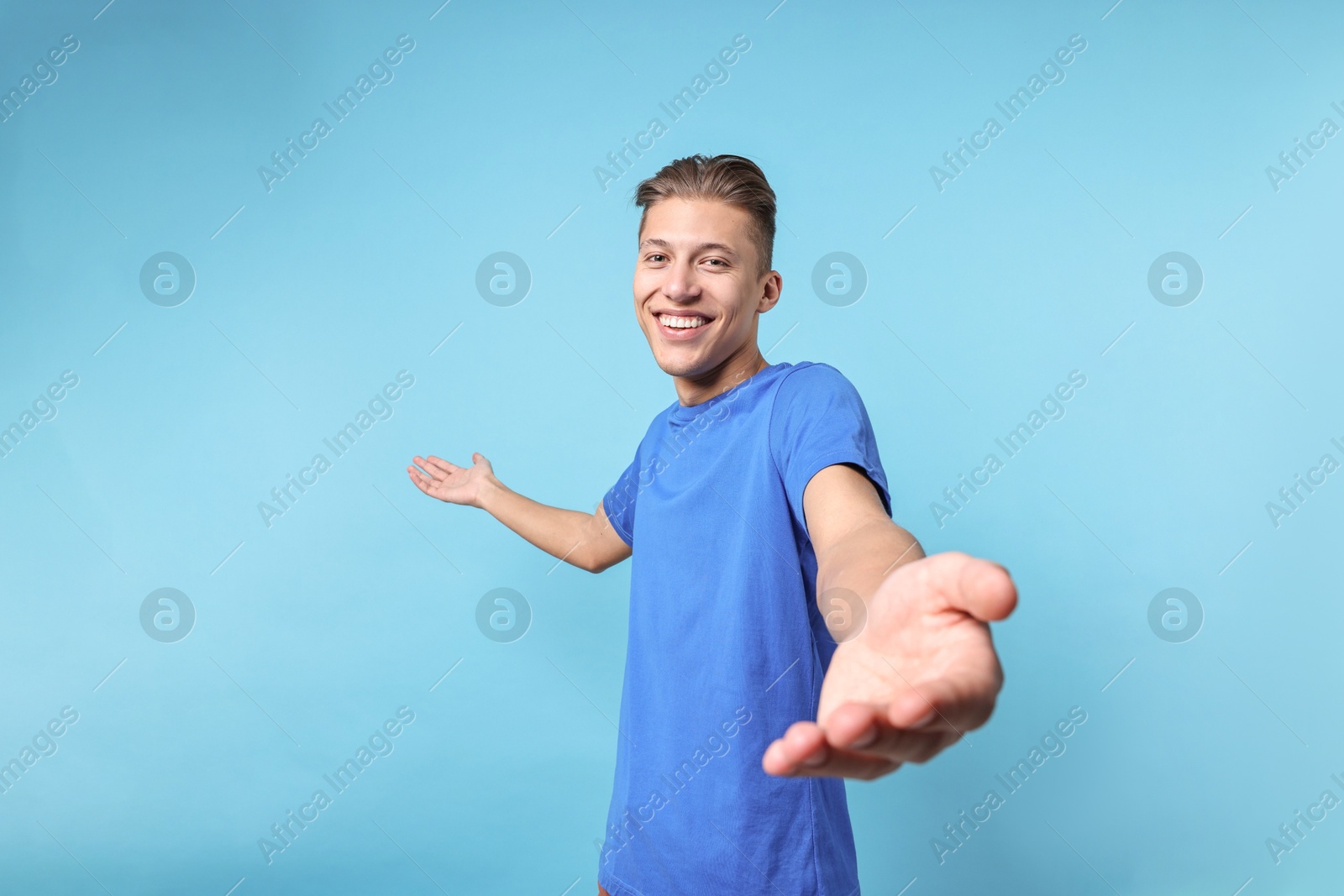 Photo of Happy man welcoming friends or guests on light blue background