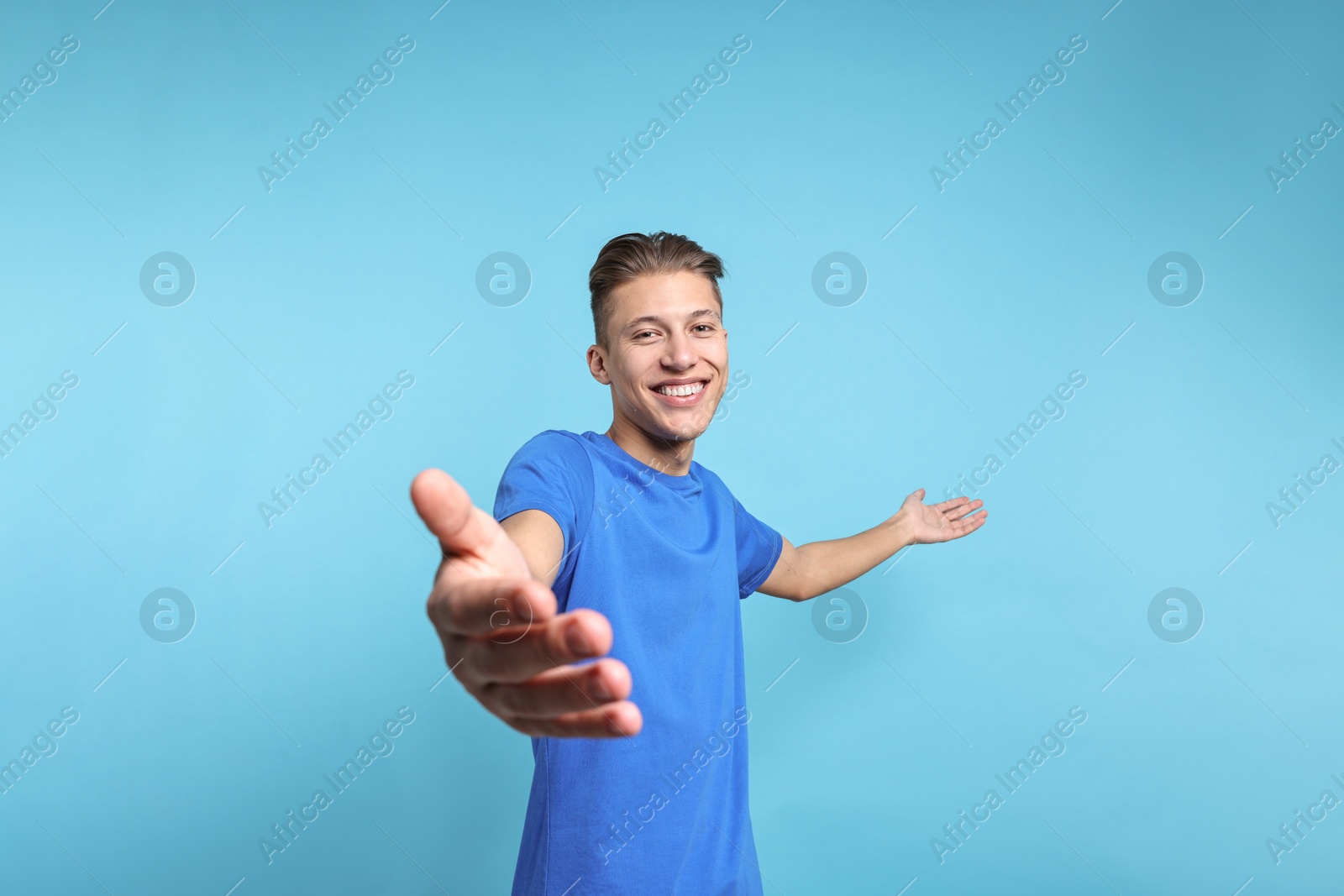 Photo of Happy man welcoming friends or guests on light blue background