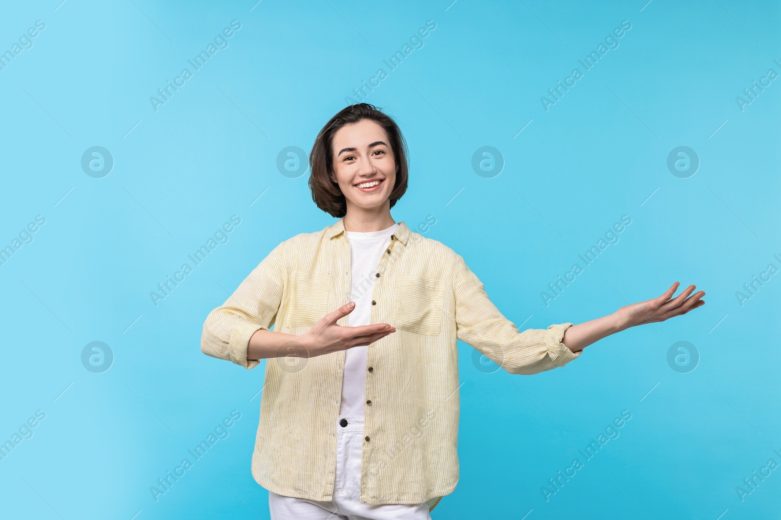 Photo of Cheerful woman welcoming friends or guests on light blue background