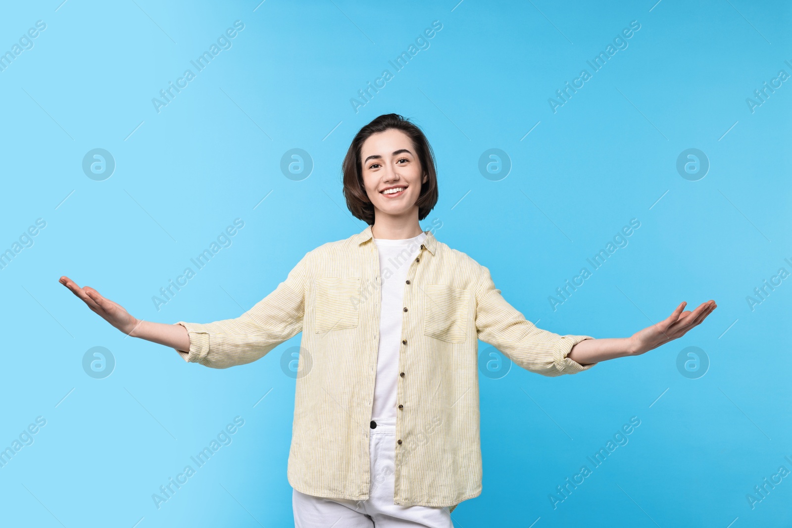 Photo of Cheerful woman welcoming friends or guests on light blue background