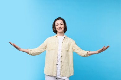 Photo of Cheerful woman welcoming friends or guests on light blue background